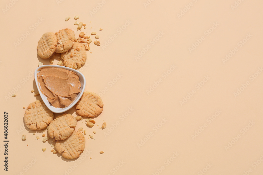 Tasty peanut cookies and bowl with butter on beige background