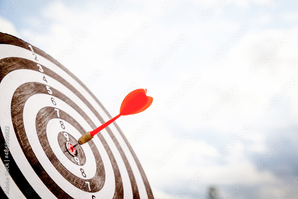 Close up shot red darts arrows in the target  of dartboard center on dark blue sky background. Busin