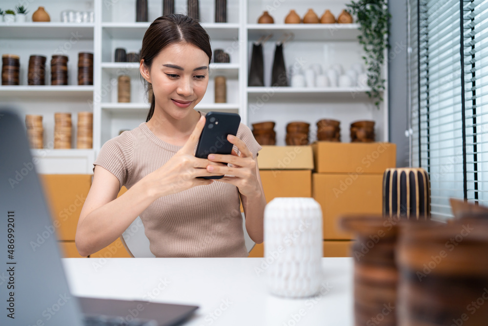 Asian business woman use mobile phone chat to check vase product order. 