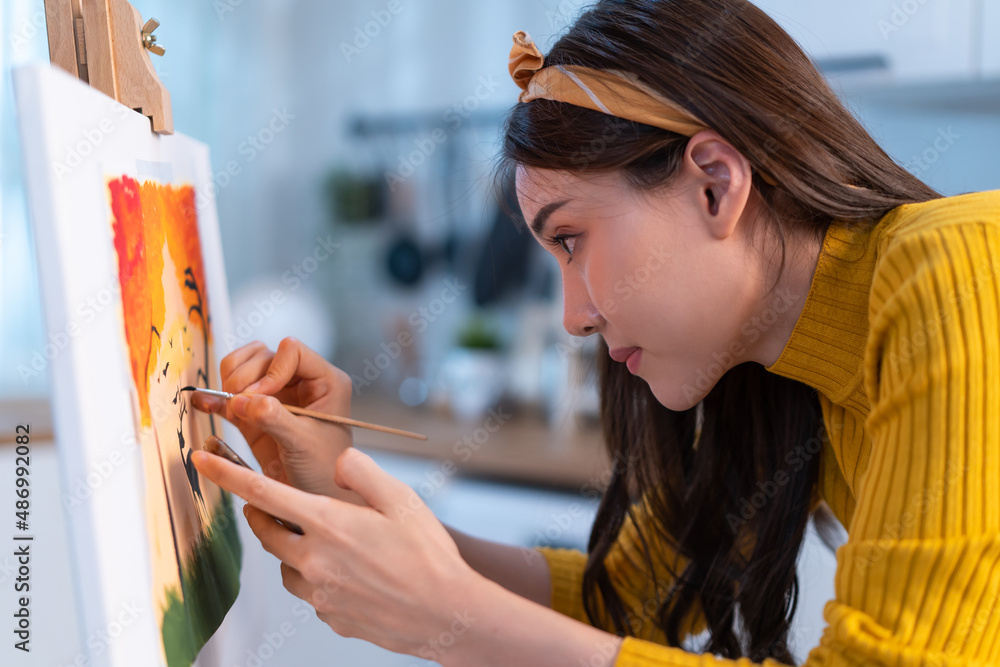 Asian young talented woman artist coloring on painting board in house. 