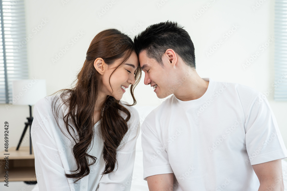 Portrait of Asian young couple sitting on bed and look at each other. 