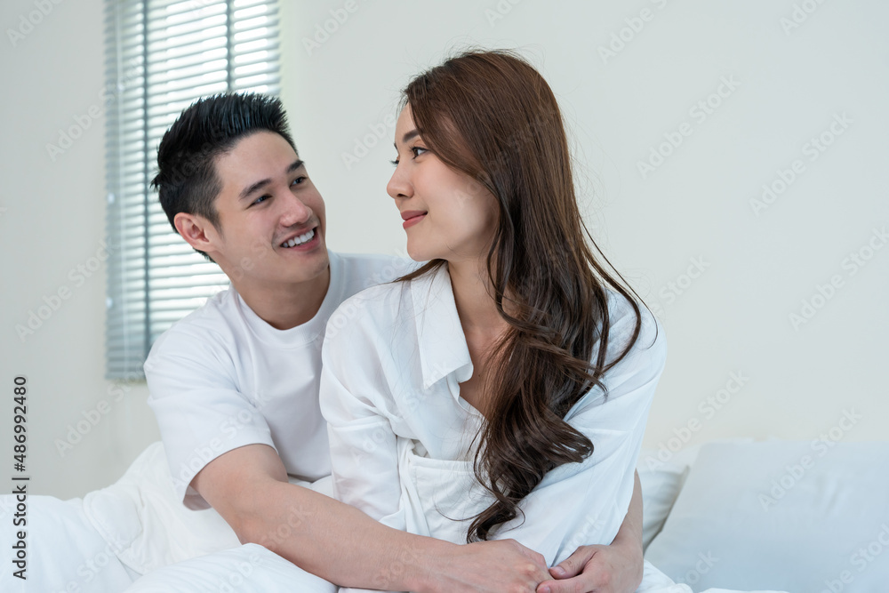 Asian new marriage couple sit on bed and look at each other with love. 