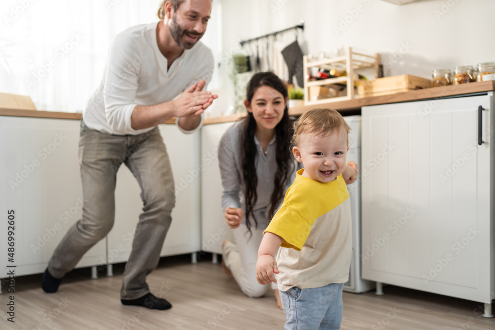 Caucasian baby boy child learn to walk with parents support in house. 