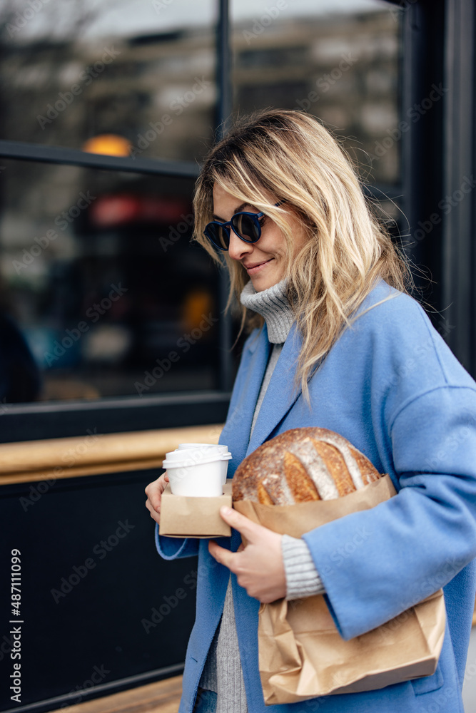 Relaxed adult woman with sunglasses, walking in the street, picking up her work lunch.