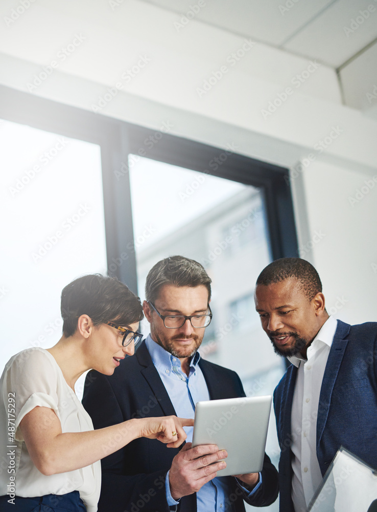 Teamwork and technology - invaluable business assets. Shot of a team of colleagues using a digital t