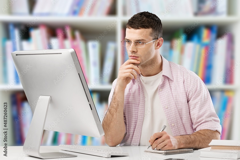 Young male student watching education webinar using laptop writing notes doing research on the inter