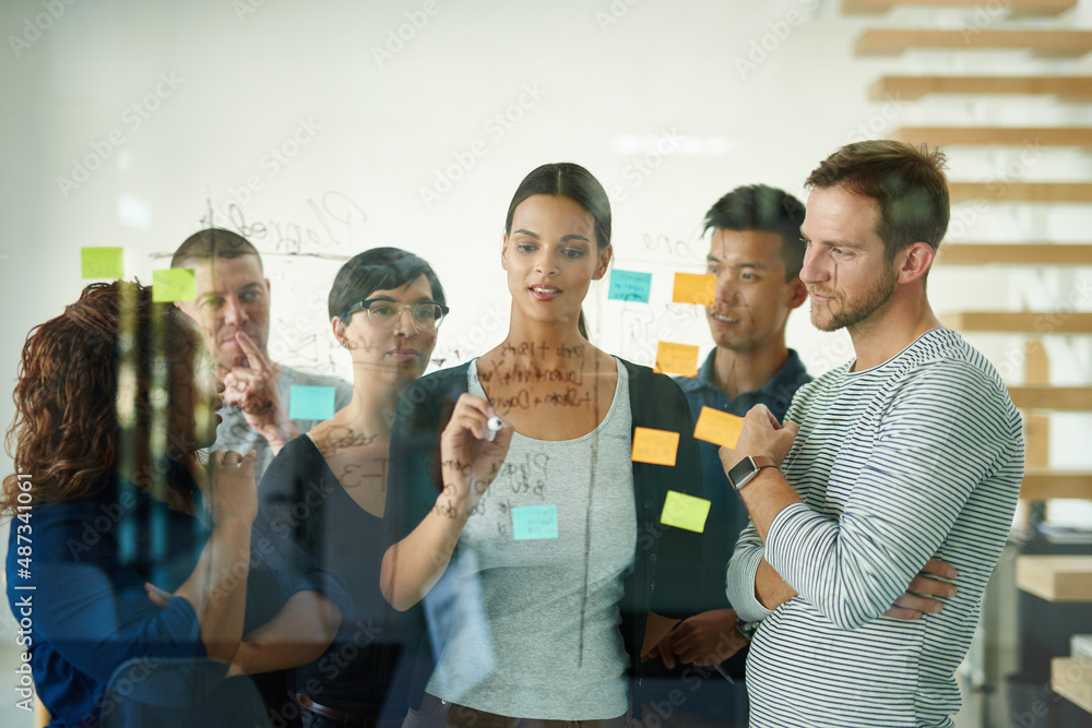 Planning is the first step. Cropped shot of a group of young designers planning on a glass board.