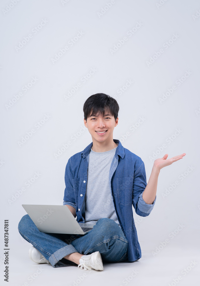 Young Asian man sitting and using laptop on white background