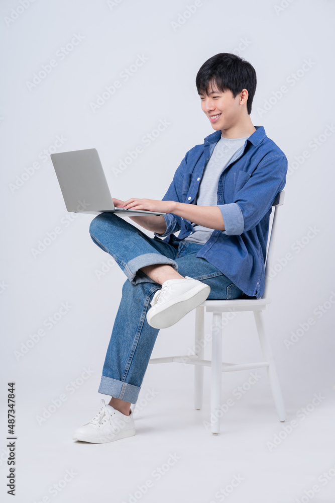 Young Asian man sitting and using laptop on white background