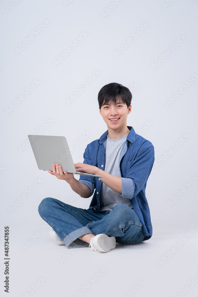 Young Asian man sitting and using laptop on white background