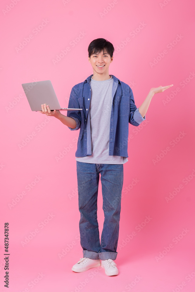 Young Asian man standing and using laptop on pink background