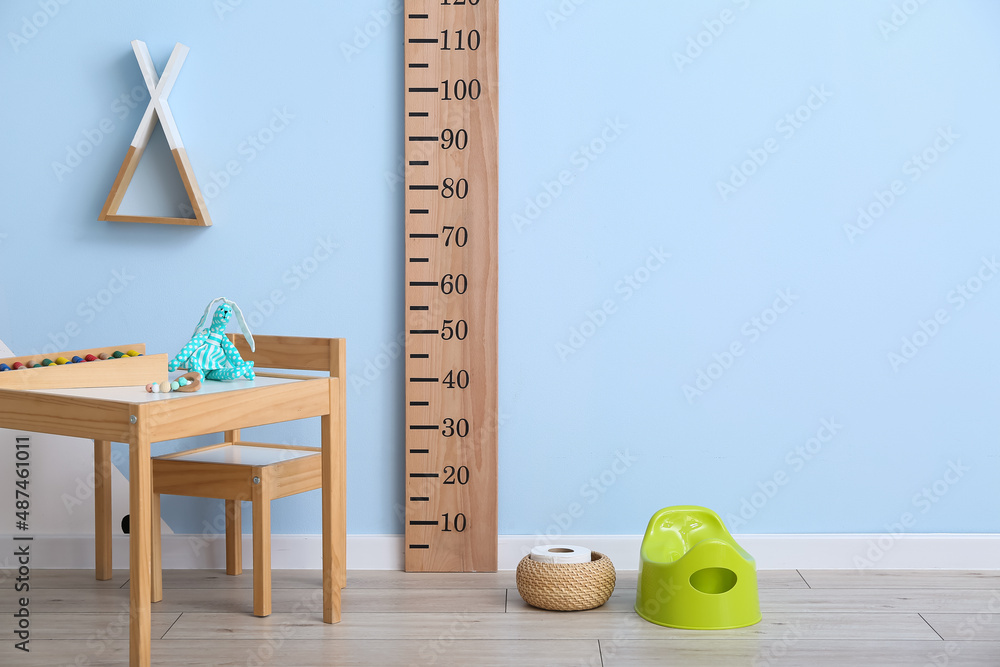 Wooden table with chair, ruler, toilet paper roll and green potty near color wall