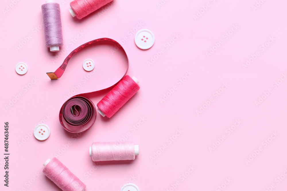 Sewing threads with measuring tape and buttons on pink background