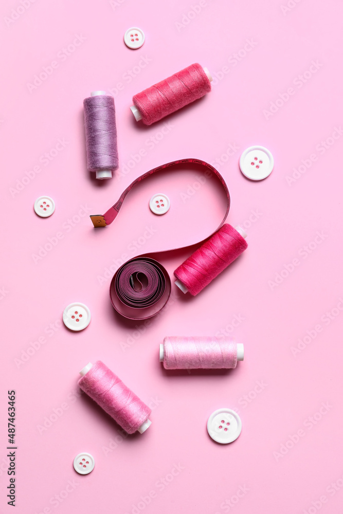 Sewing threads with measuring tape and buttons on pink background