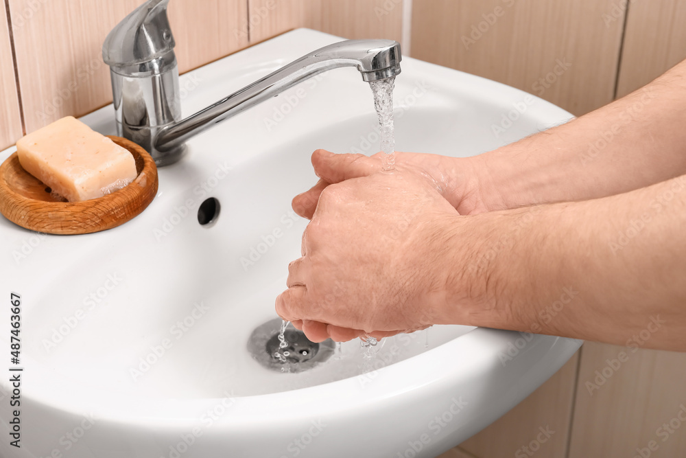 Man washing his hands under running water from tap in bathroom, closeup