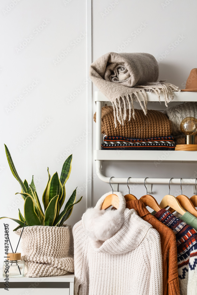 Rack with stylish sweaters and ear muffs near light wall