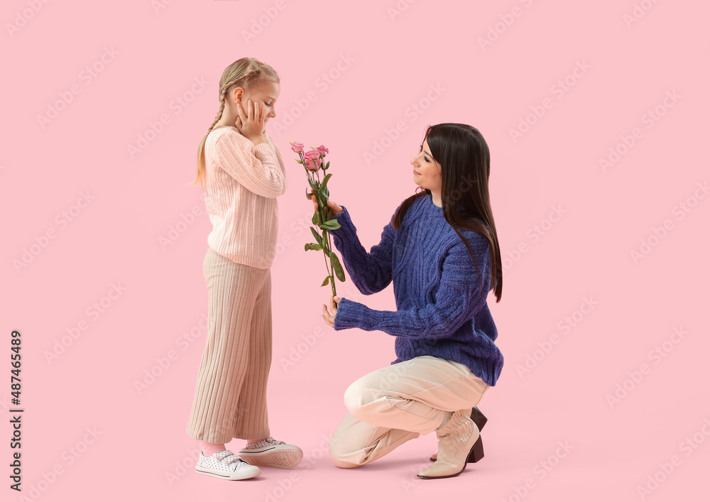 Happy mother greeting her little daughter with tulip flowers on pink background