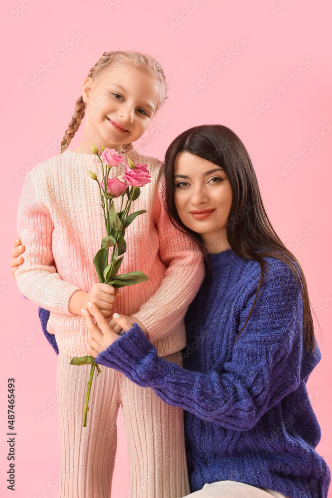 Little girl with flowers and her mother in warm sweaters on pink background