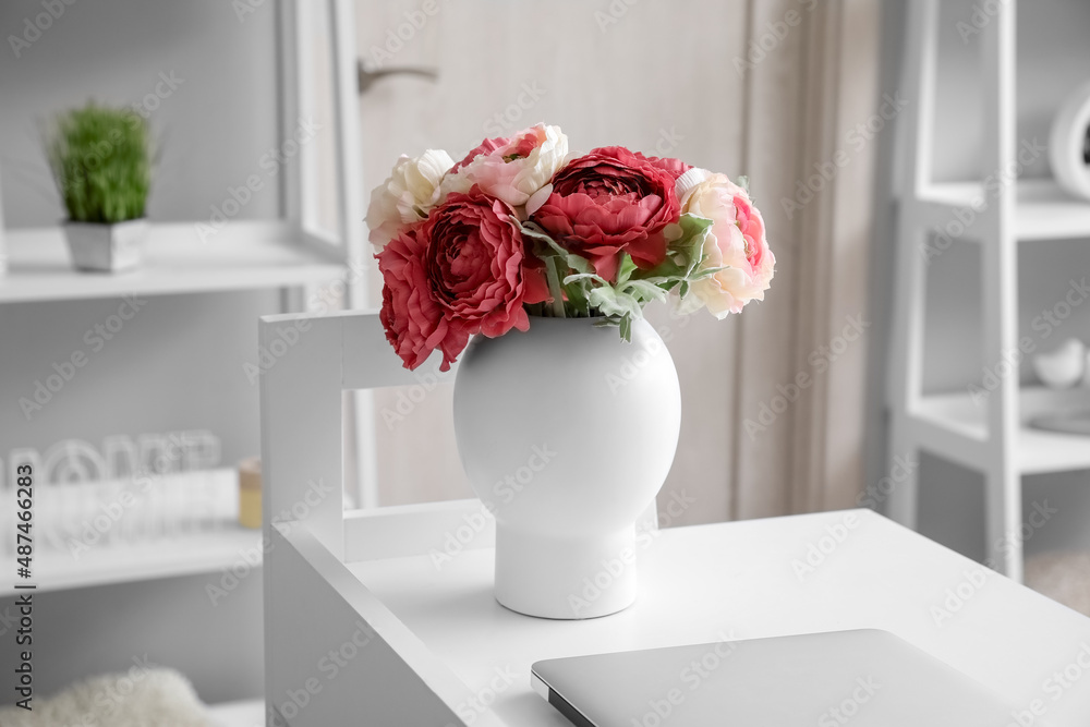 Vase with flowers and laptop on table in light room