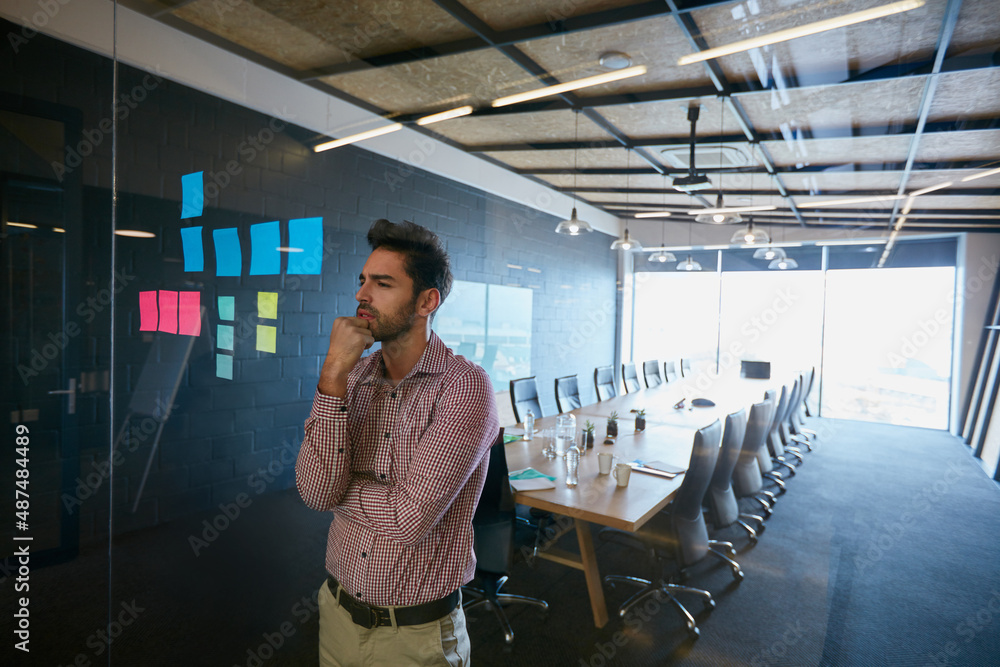 Design is thinking made visible. Shot of a young businessman looking at sticky notes on a glass wall