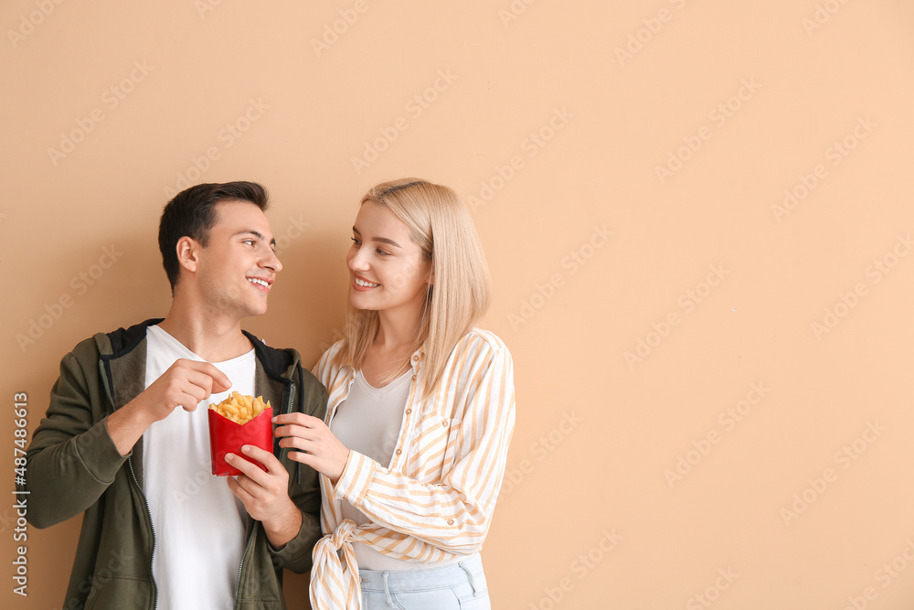 Happy young couple with french fries on beige background