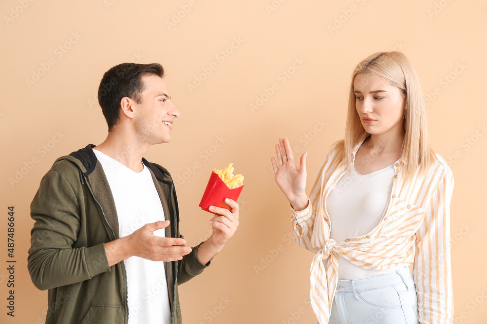 Young woman refusing to eat french fries on beige background