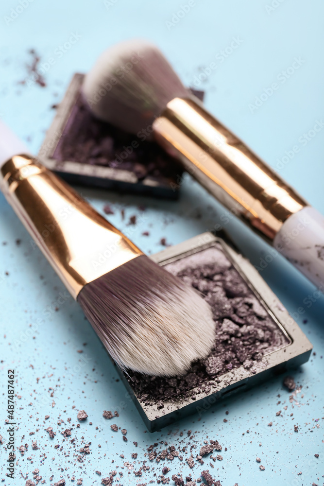 Makeup brushes and eye shadow palettes on color background