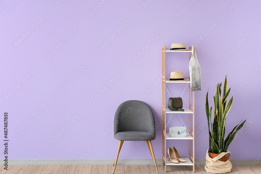 Shelving unit with accessories, chair and houseplant near lilac wall