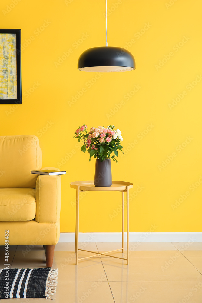 Vase with bouquet of beautiful fresh roses on table near yellow wall