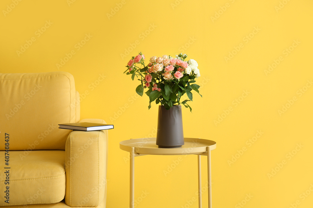 Vase with bouquet of beautiful fresh roses on table near yellow wall