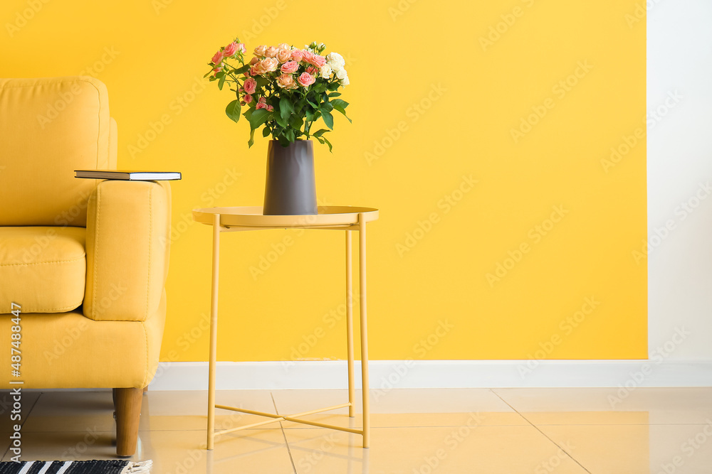 Vase with bouquet of beautiful fresh roses on table near yellow wall