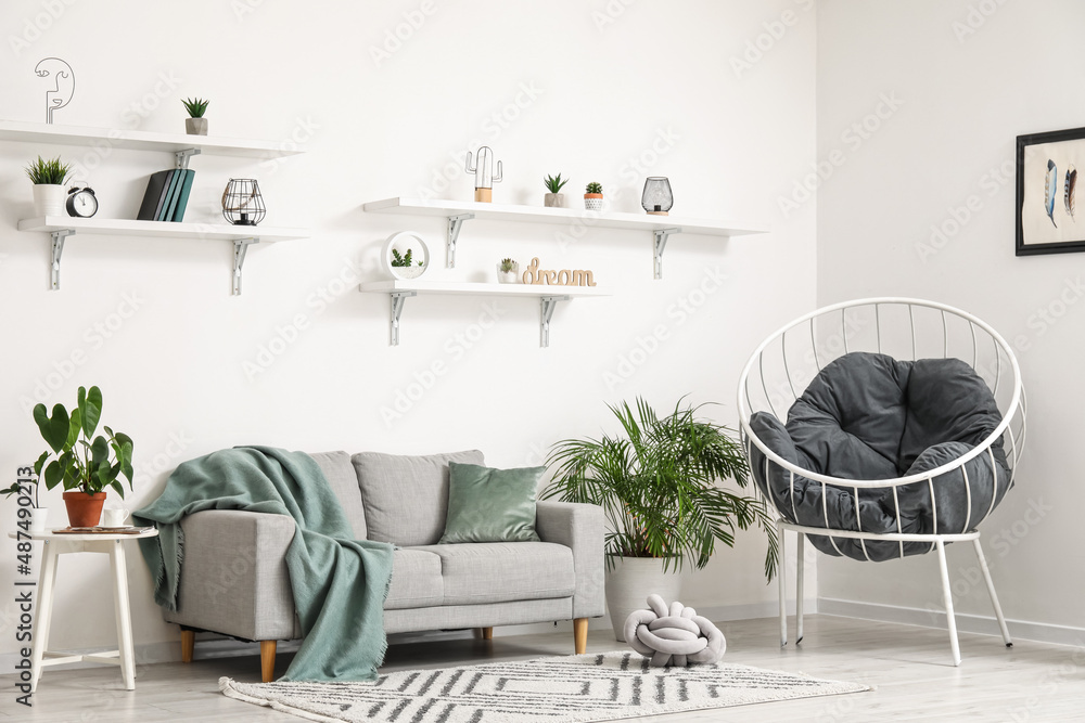 Interior of light living room with grey sofa, armchair and houseplants