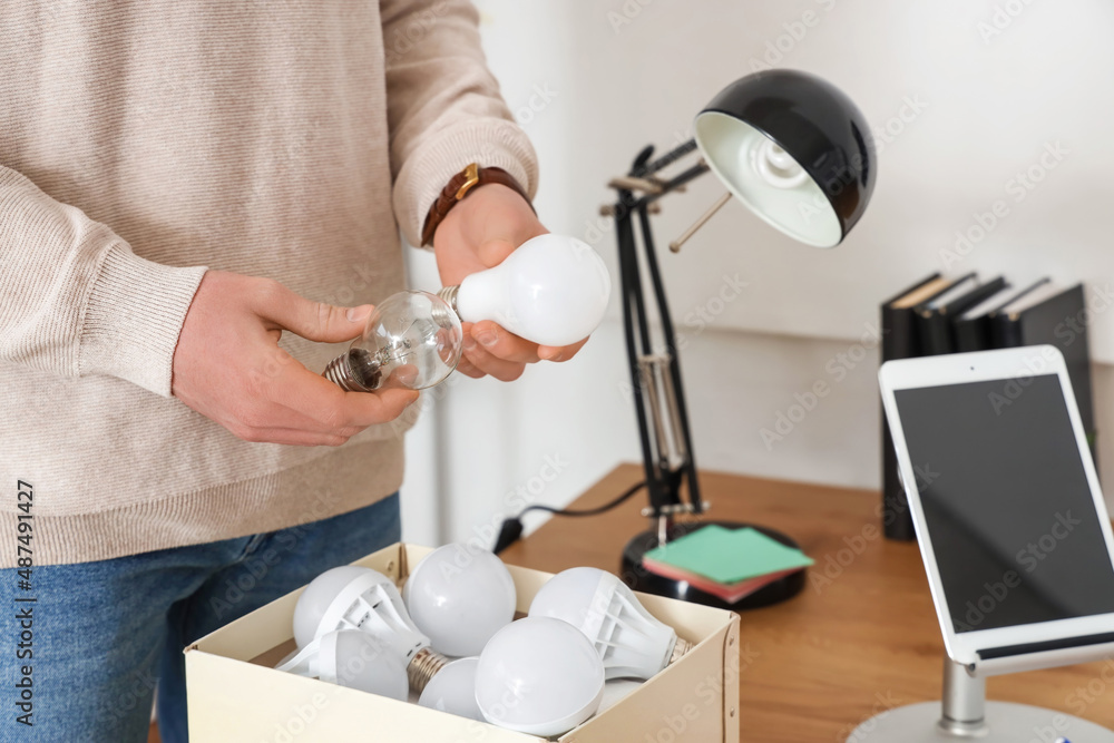 Man with different light bulbs at desk in office, closeup