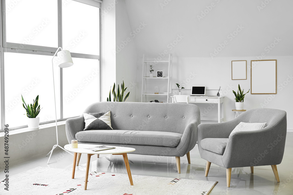 Interior of light living room with grey sofa, armchair and table