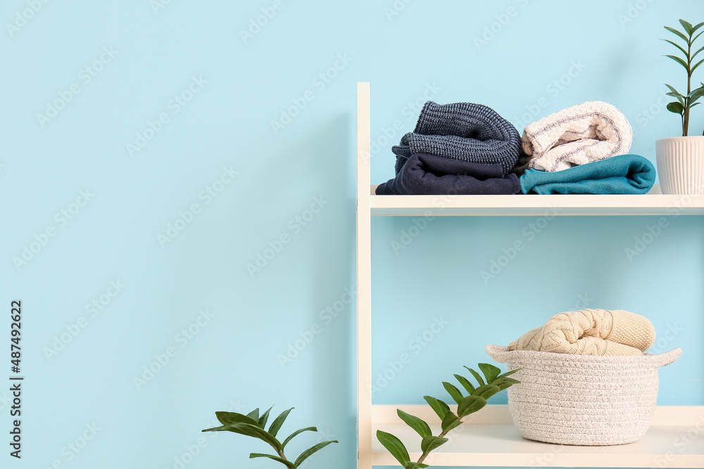 Shelf unit with knitted sweaters and houseplant near blue wall