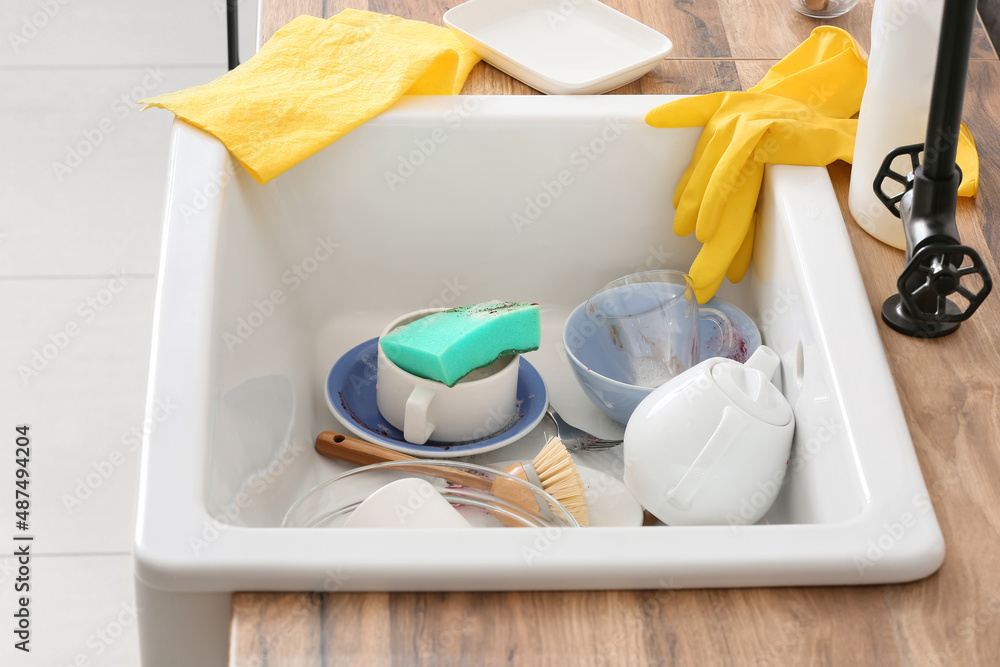 Dirty dishes, cleaning sponge and brush in ceramic sink