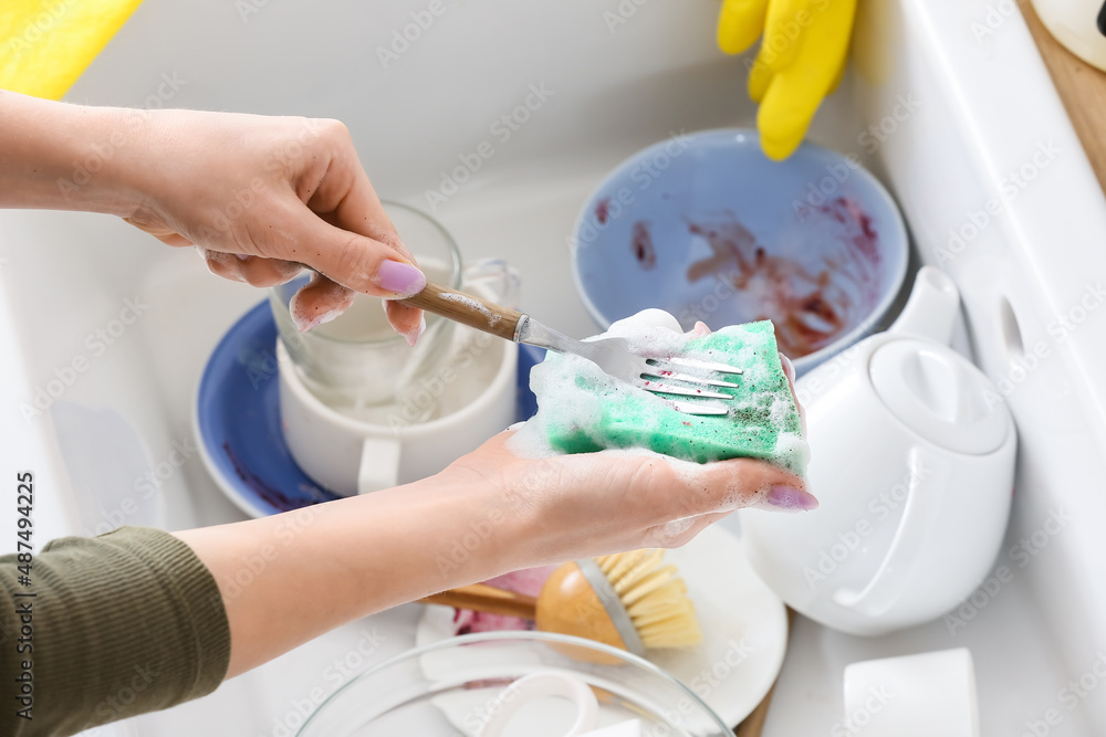 Woman washing fork with sponge over sink, closeup