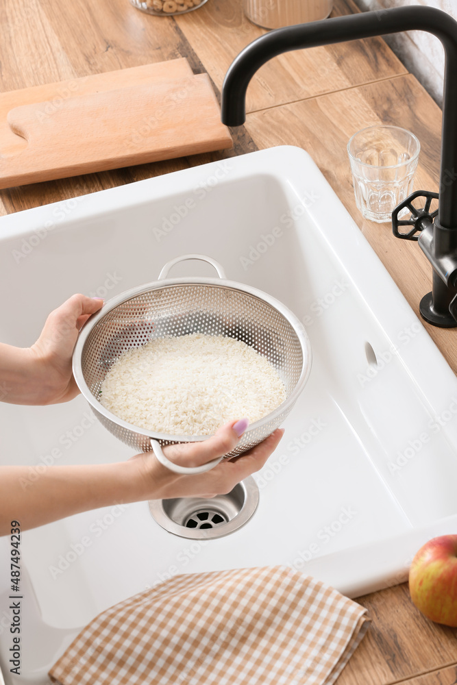 Woman holding colander with raw rice over sink, closeup