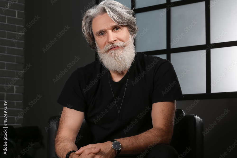 Portrait of handsome mature bearded man sitting in armchair at home