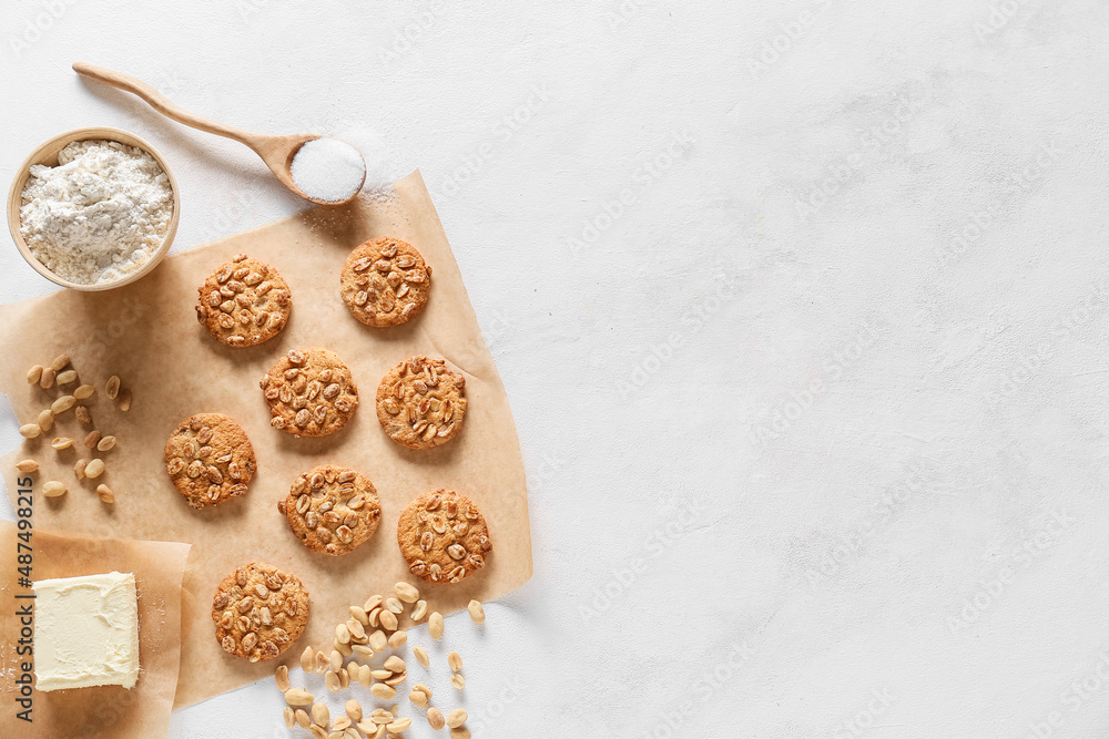 Parchment paper with tasty peanut cookies and ingredients on white background