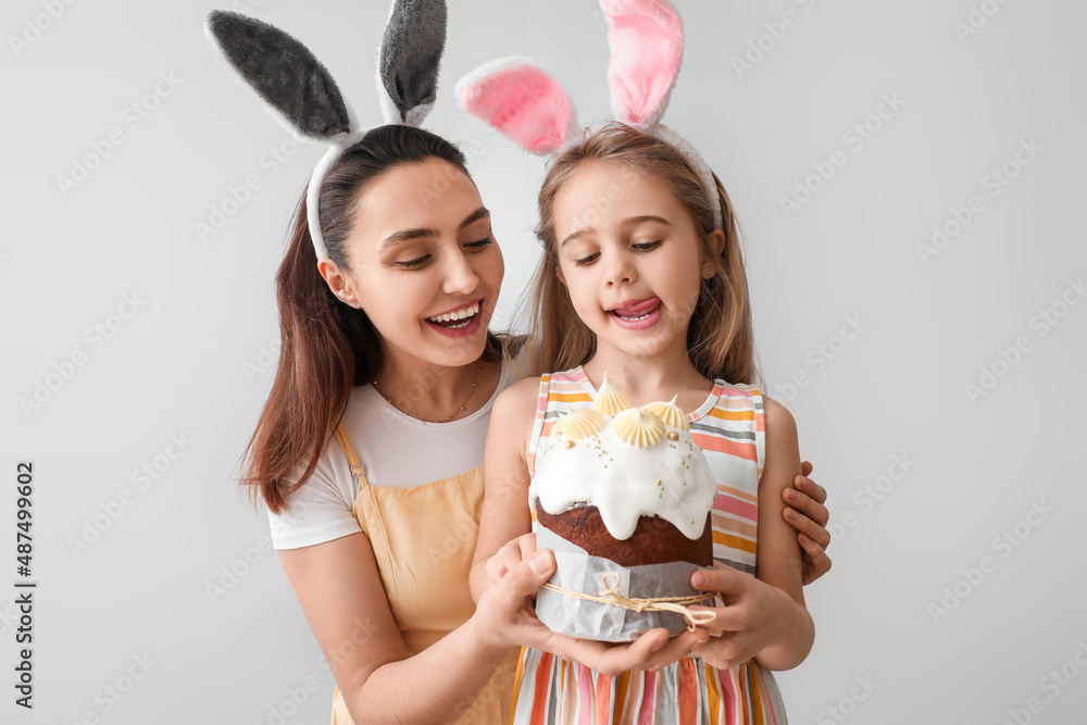 Little girl and her mother in bunny ears with Easter cake on light background