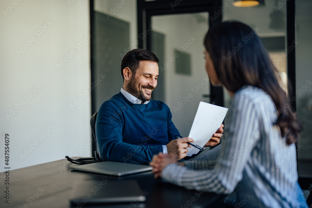 Smiling caucasian man, reading a document his coworker brought him.