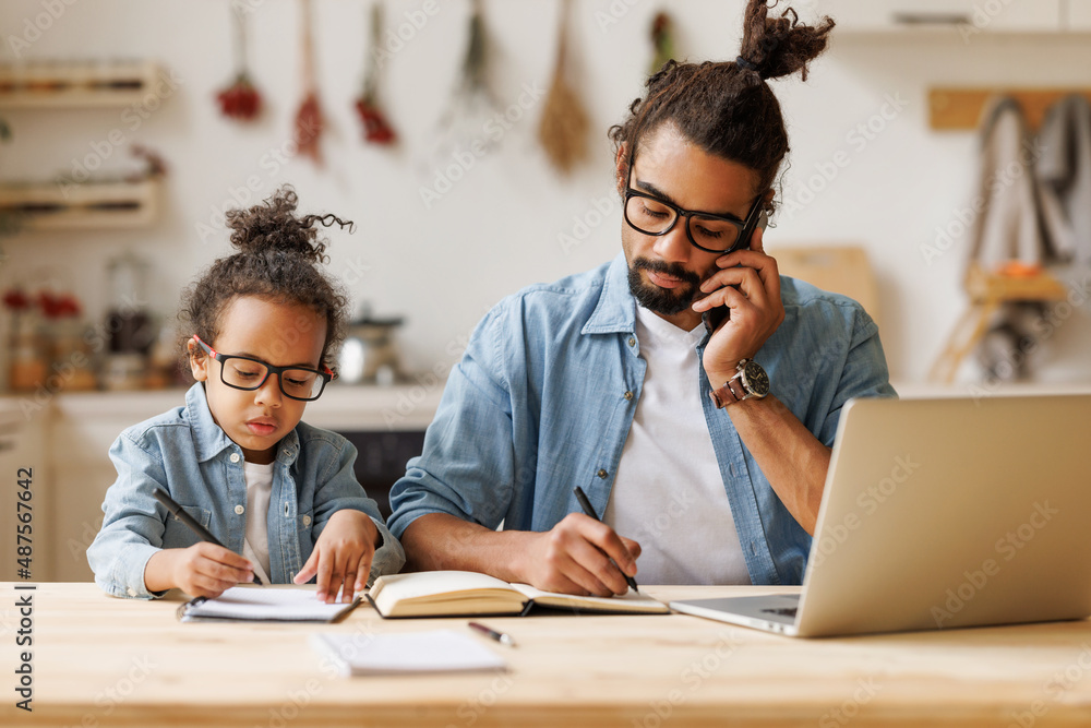 Young african american dad working remotely on laptop with child son at home