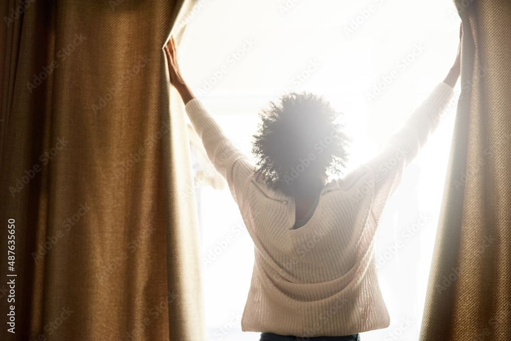 New day, new possibilities. Rearview shot of a woman opening the curtains on a bright sunny day.