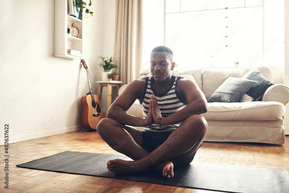 Your thoughts control your life. Shot of a sporty young man meditating at home.