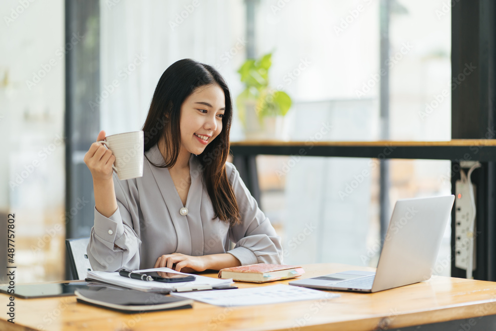 年轻女商人坐在办公室的电脑前，在笔记本上做笔记的肖像。