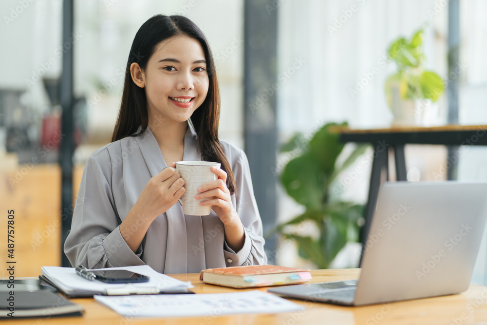 Portrait of young businesswoman sitting in office in front of computer and taking notes in notebook.