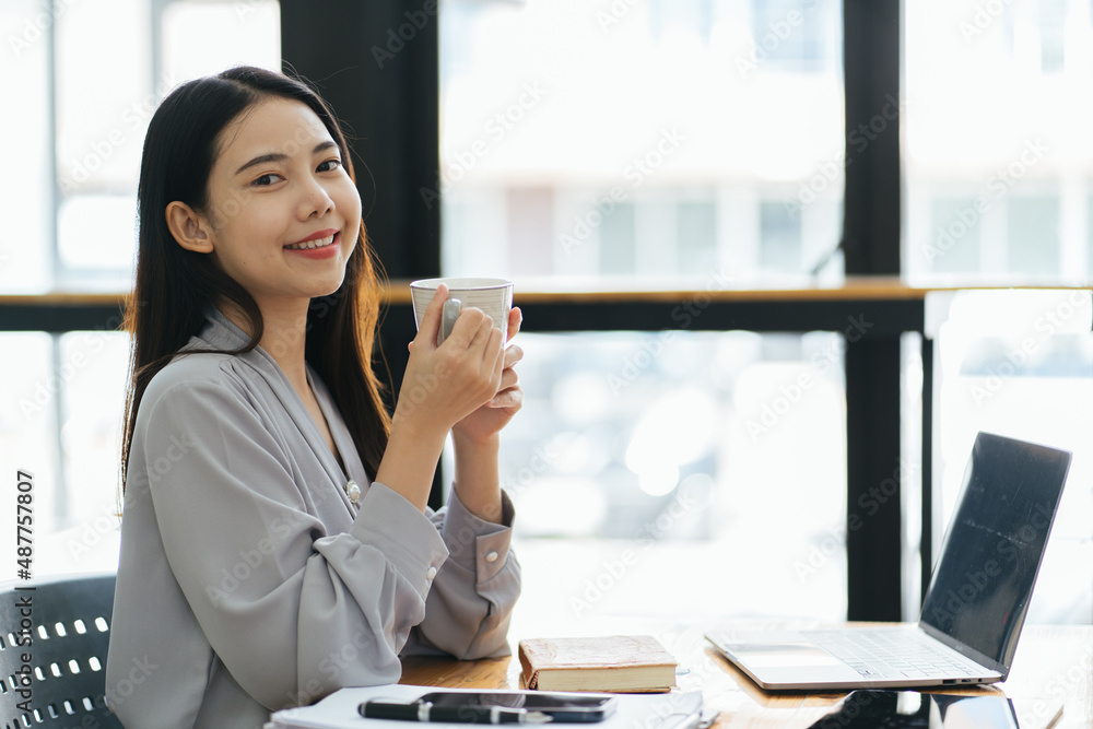 年轻女商人坐在办公室的电脑前，在笔记本上做笔记的肖像。