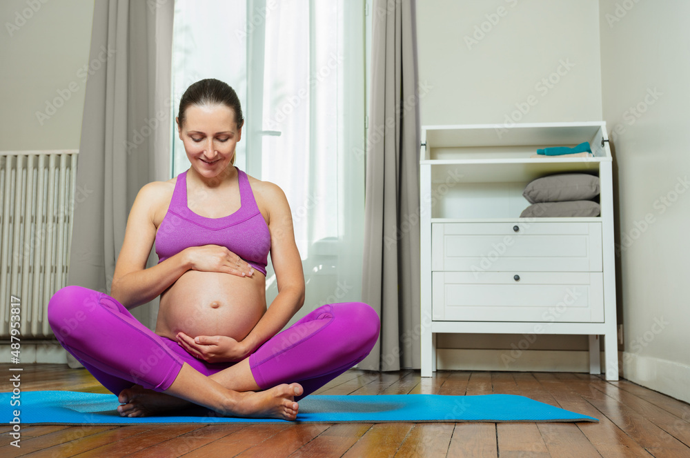 Pregnant in sport clothes hold belly on yoga mat