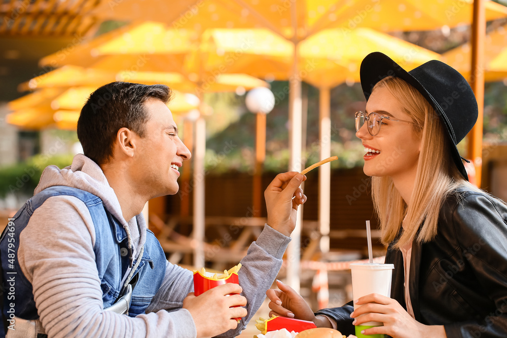 Young couple eating french fries in cafe outdoors